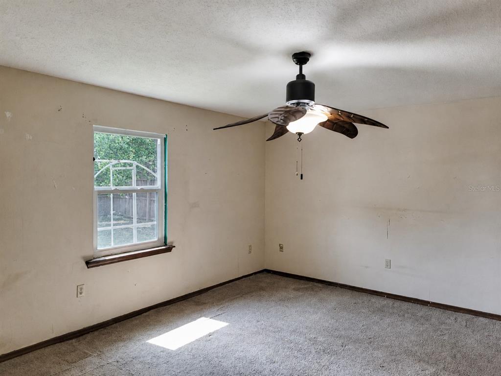 An empty bedroom features beige walls, carpeted flooring, and a ceiling fan with leaf-shaped blades — 726 DIPLOMAT AVENUE SE, PALM BAY, FL