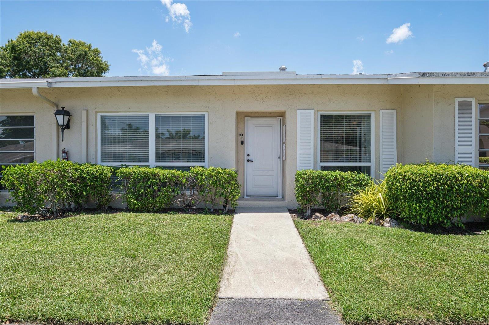 A single-story residential building with a white front door, large windows, and manicured landscaping — 13725 Flora Place # C, Delray Beach FL 33484, DELRAY BEACH, FL
