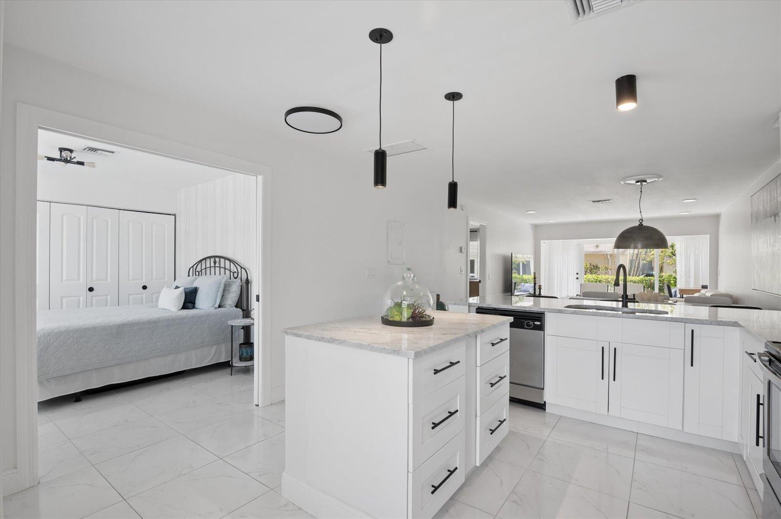 A white kitchen with a marble-topped island and pendant lights opens into a bedroom — 13725 Flora Place # C, Delray Beach FL 33484, DELRAY BEACH, FL