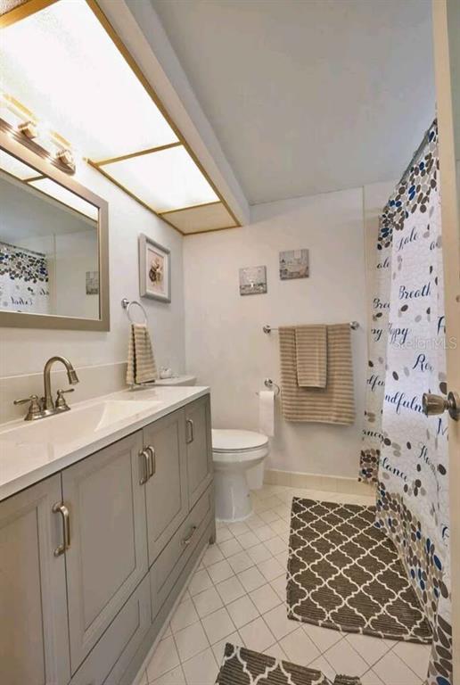 A bathroom features a gray vanity, a toilet, and a shower with a patterned curtain — 4550 COVE CIRCLE UNIT 808, ST PETERSBURG, FL