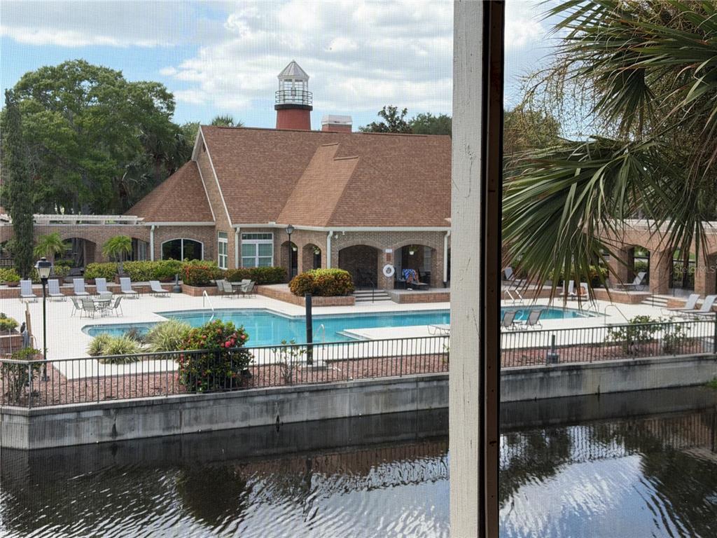 A view from a screened porch overlooking a swimming pool, a canal, and a clubhouse — 10200 GANDY BOULEVARD N UNIT 1316, ST PETERSBURG, FL