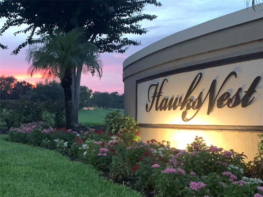 A curved stone monument sign for Hawks Nest stands beside a garden at sunset — 7291 HAWKSNEST BOULEVARD, ORLANDO, FL
