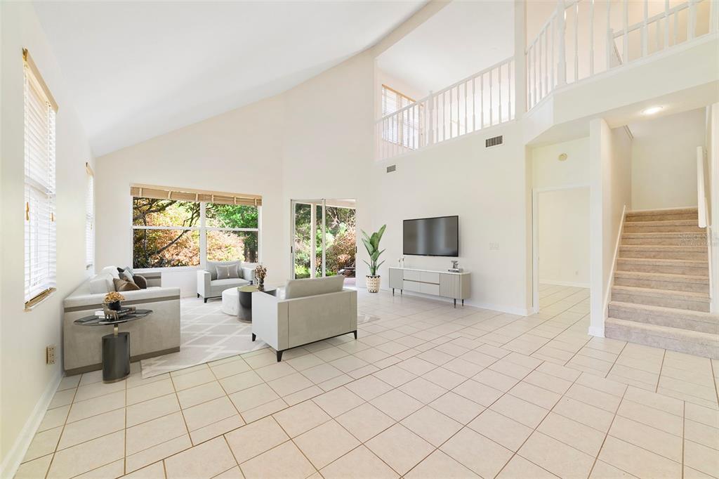 A bright living room features vaulted ceilings, tile flooring, a staircase, and a loft overlook — 7291 HAWKSNEST BOULEVARD, ORLANDO, FL