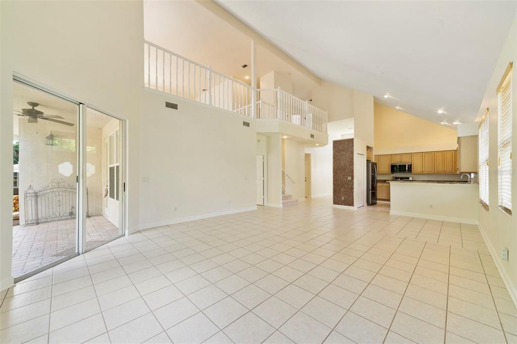 A spacious living room with tile floors, vaulted ceilings, a loft balcony, and an open kitchen — 7291 HAWKSNEST BOULEVARD, ORLANDO, FL
