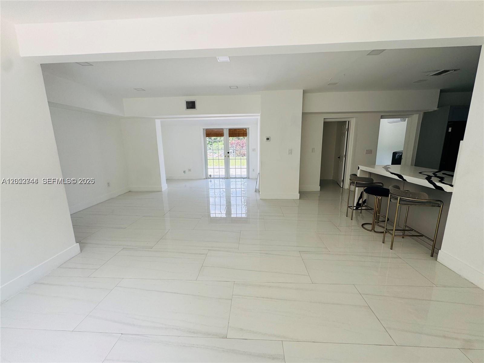An open-concept living area features white tile floors, a kitchen island, and glass patio doors — 516 La Villa Dr, Miami Springs FL 33166, MIAMI SPRINGS, FL