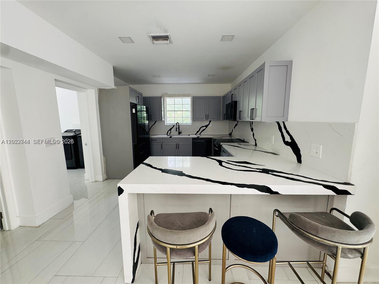 A kitchen features gray cabinets, white marble-patterned countertops with bold black veining, and bar stools — 516 La Villa Dr, Miami Springs FL 33166, MIAMI SPRINGS, FL