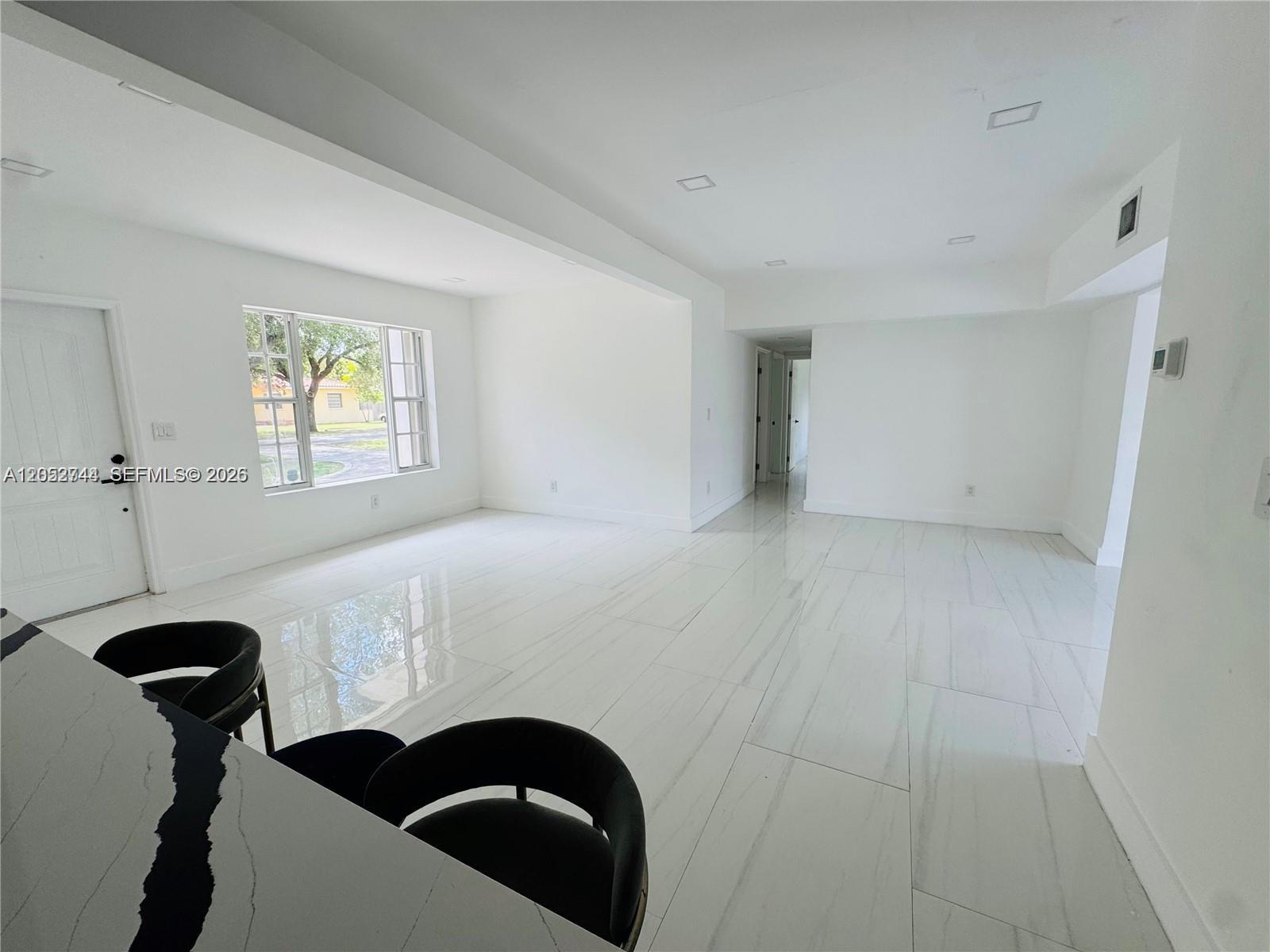 A bright, empty room features white walls, polished tile flooring, and a kitchen island counter — 516 La Villa Dr, Miami Springs FL 33166, MIAMI SPRINGS, FL