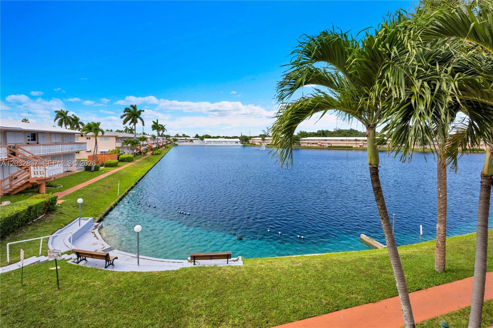 An exterior view of a residential complex featuring a lake, palm trees, and walkways — 1050 SW 11th ST # 20L, Hallandale Beach FL 33009, HALLANDALE BEACH, FL