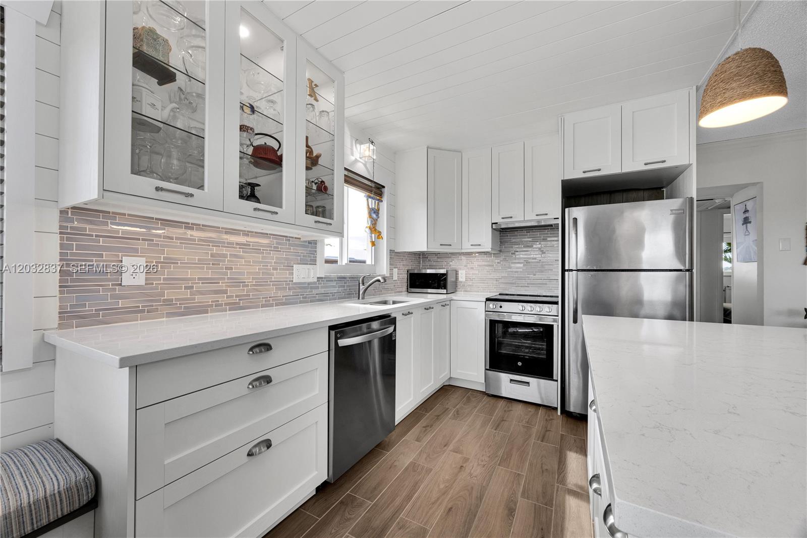 A modern kitchen features white cabinetry, stainless steel appliances, quartz countertops, and wood-look tile flooring — 1050 SW 11th ST # 20L, Hallandale Beach FL 33009, HALLANDALE BEACH, FL