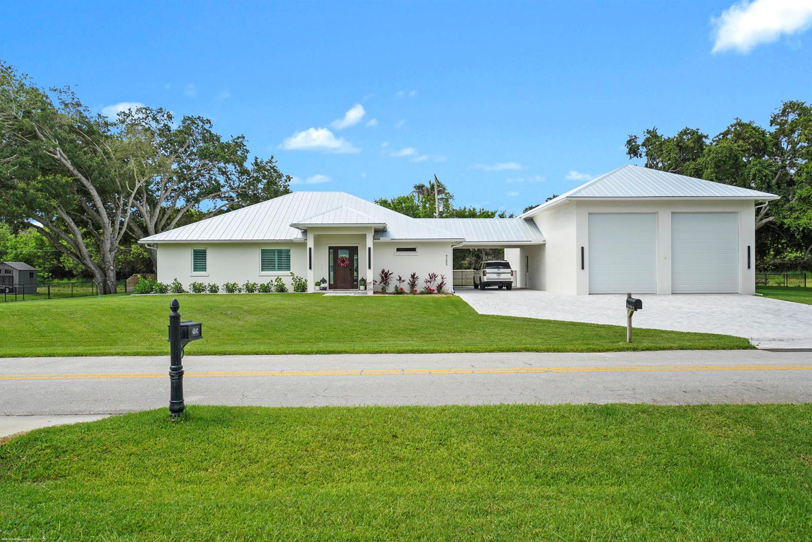 A white single-story house with a metal roof, attached garage, and a large front lawn — 4255 79th Street, Vero Beach FL 32967, VERO BEACH, FL