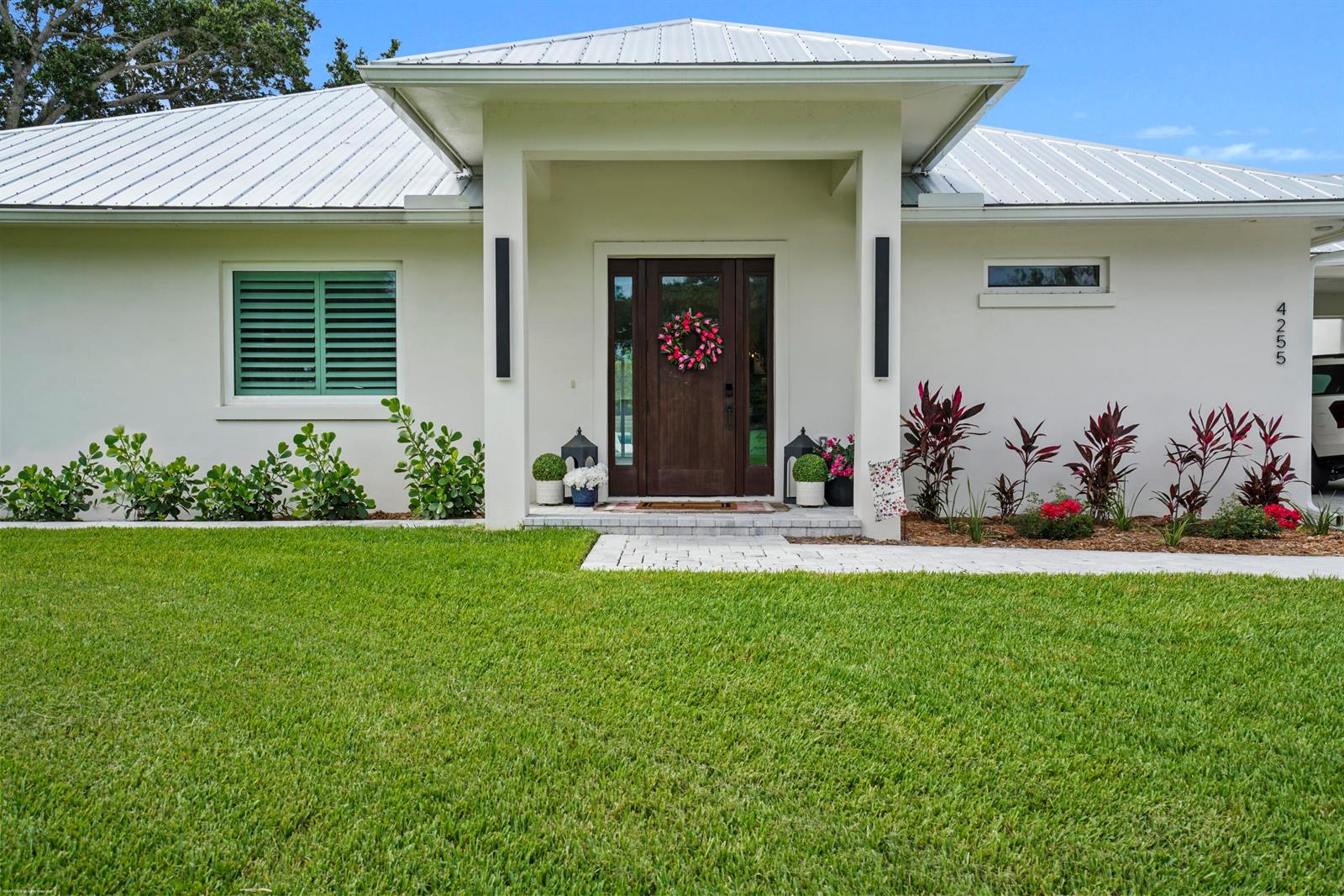 The exterior of a white house features a metal roof, a wooden door, and landscaping — 4255 79th Street, Vero Beach FL 32967, VERO BEACH, FL