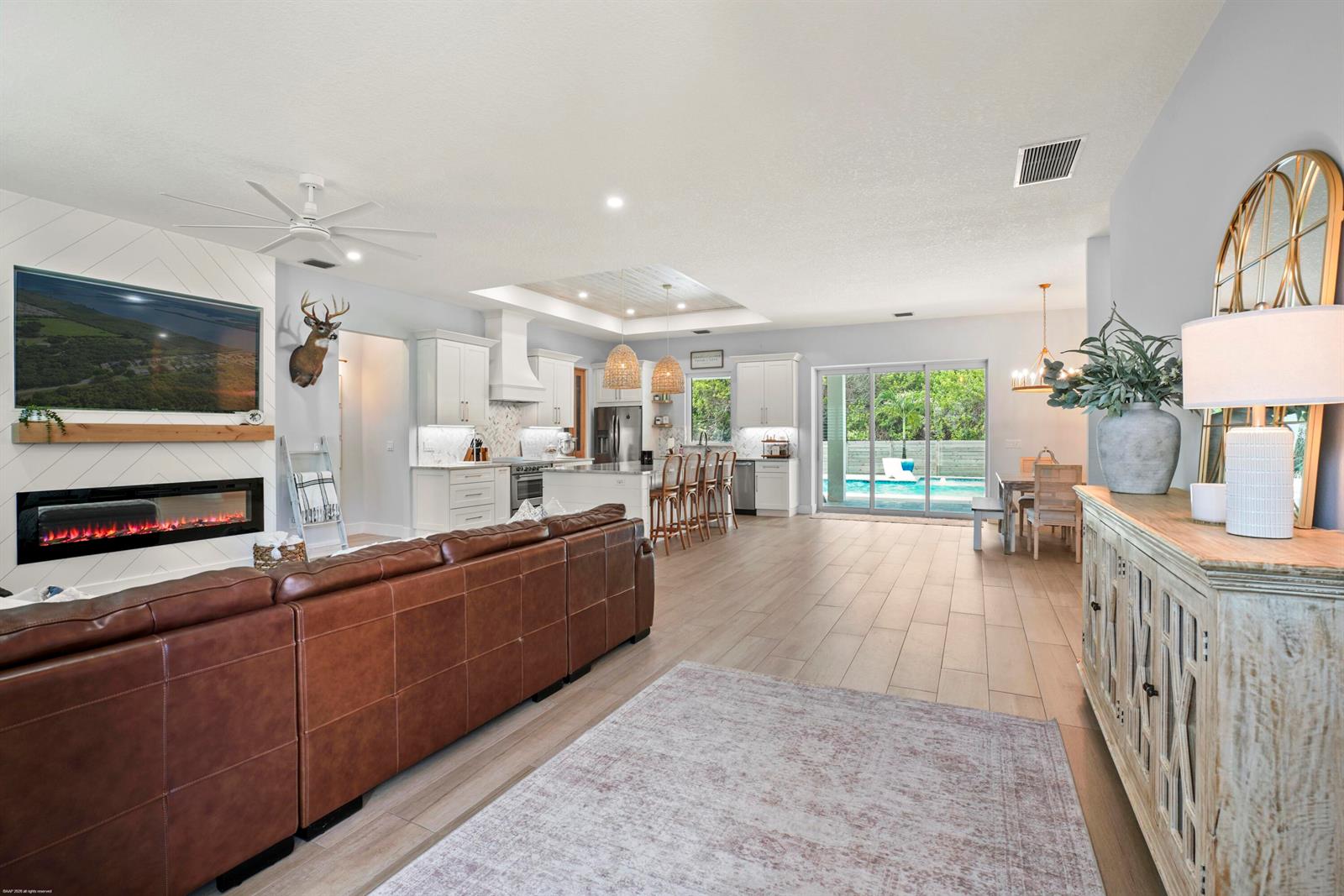 An open-concept living room and kitchen with a leather sofa, fireplace, and pool view — 4255 79th Street, Vero Beach FL 32967, VERO BEACH, FL