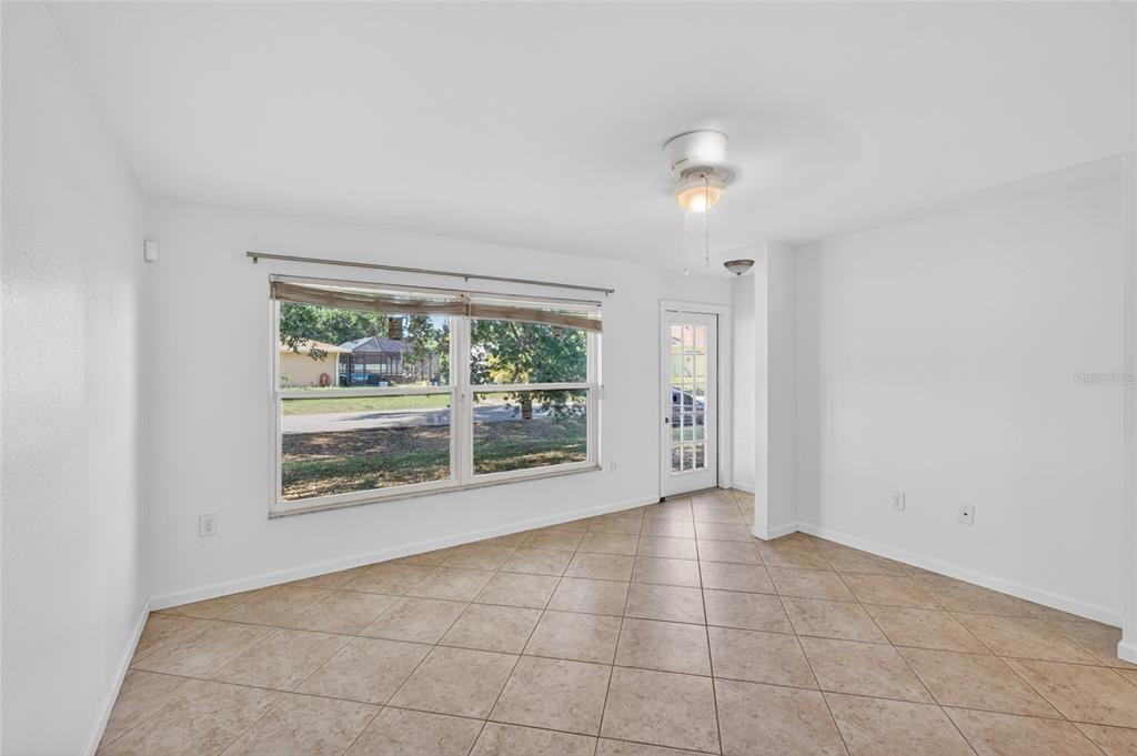 A bright, empty room features white walls, beige tile flooring, a large window, and a door — 2025 BARKSDALE STREET, PORT CHARLOTTE, FL