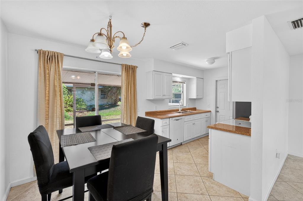 A dining area with a black table and chairs sits adjacent to a white kitchen — 2025 BARKSDALE STREET, PORT CHARLOTTE, FL