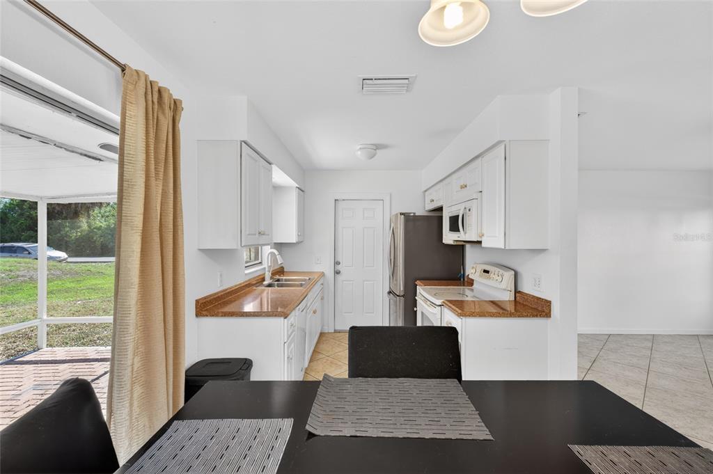 A kitchen features white cabinets, brown countertops, and a dining table in the foreground — 2025 BARKSDALE STREET, PORT CHARLOTTE, FL
