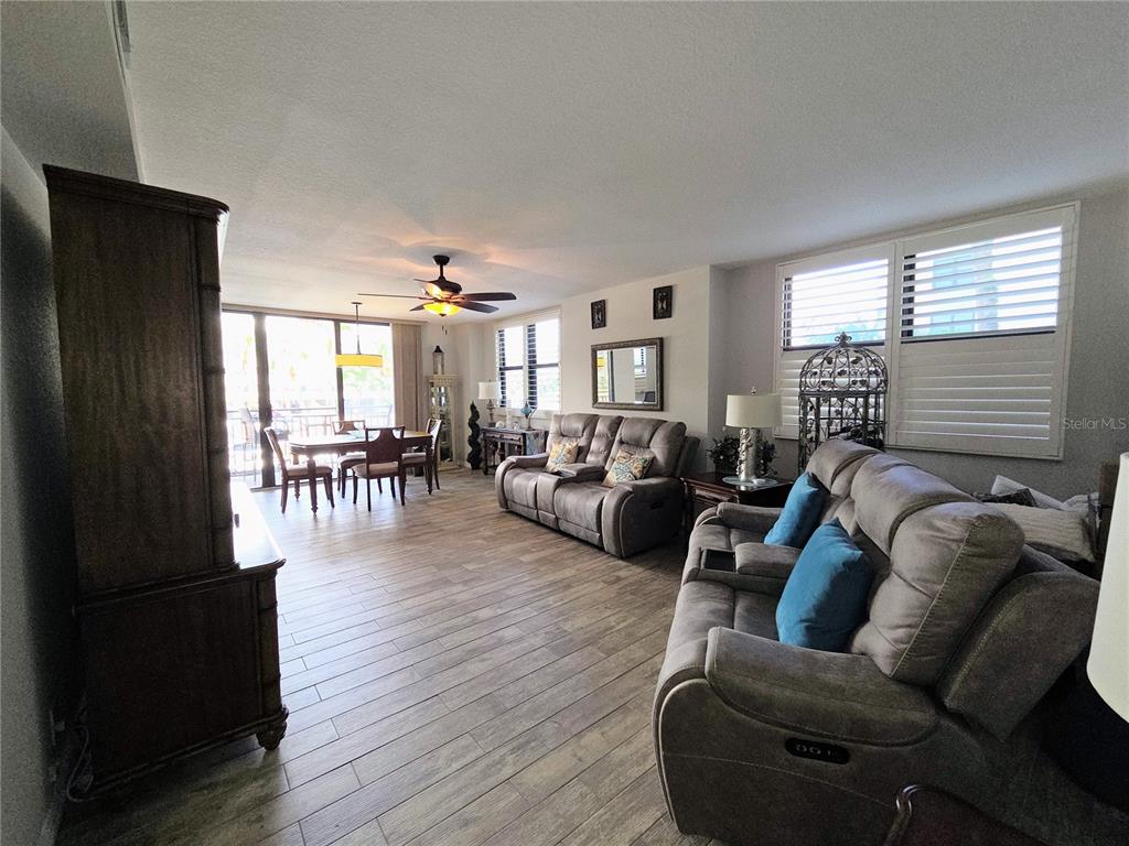 A living and dining area features wood-look tile flooring, two gray sofas, and plantation shutters — 3820 GULF BOULEVARD UNIT 108, ST PETE BEACH, FL