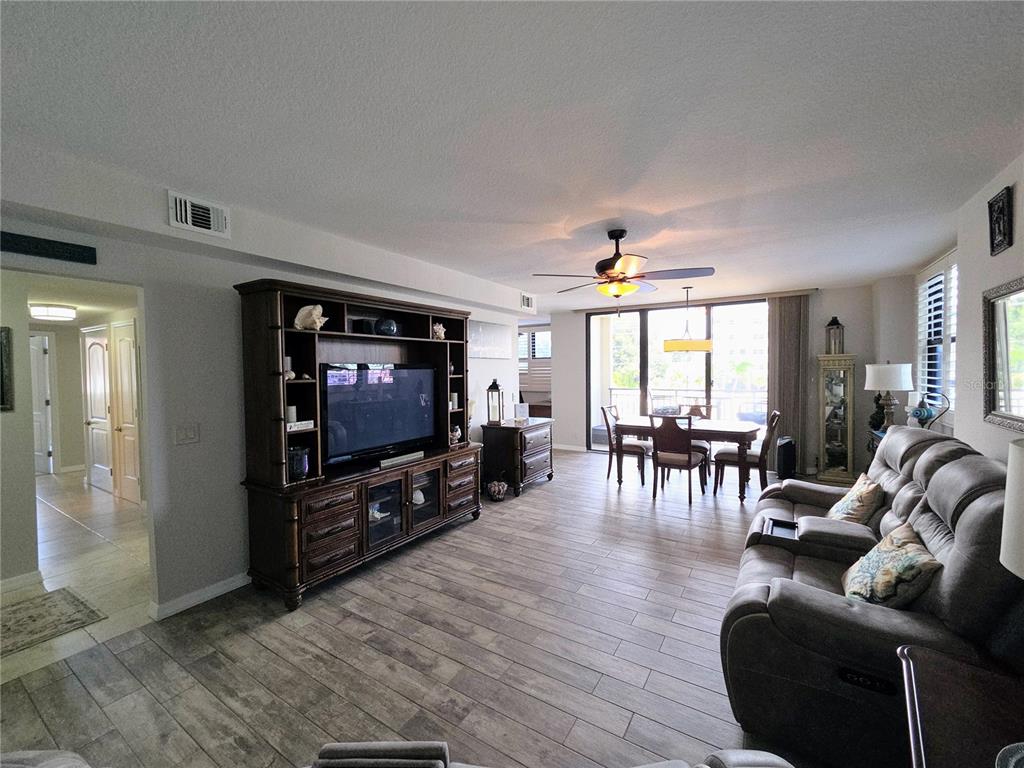 A living room features wood-look tile flooring, a large entertainment center, and a dining area — 3820 GULF BOULEVARD UNIT 108, ST PETE BEACH, FL