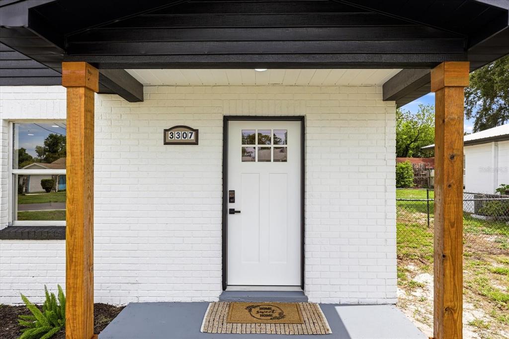 A white front door with a small window sits under a porch with wooden posts — 3307 HICKMAN AVENUE, PLANT CITY, FL