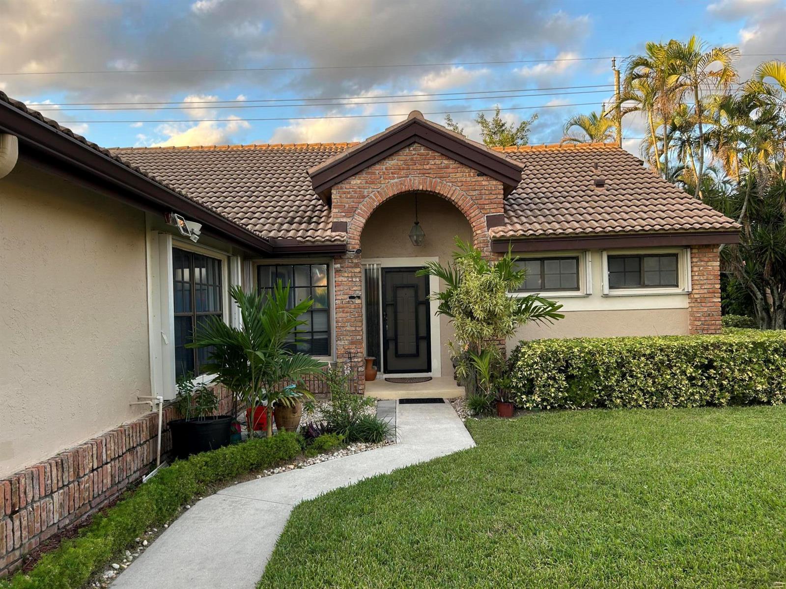 A single-story house with a brick-arched entryway, tiled roof, and a concrete walkway — 7207 Le Chalet Boulevard, Boynton Beach FL 33472, BOYNTON BEACH, FL