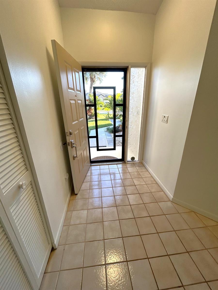 An entryway features beige tile flooring, a louvered closet door, and a glass-paneled front door — 7207 Le Chalet Boulevard, Boynton Beach FL 33472, BOYNTON BEACH, FL
