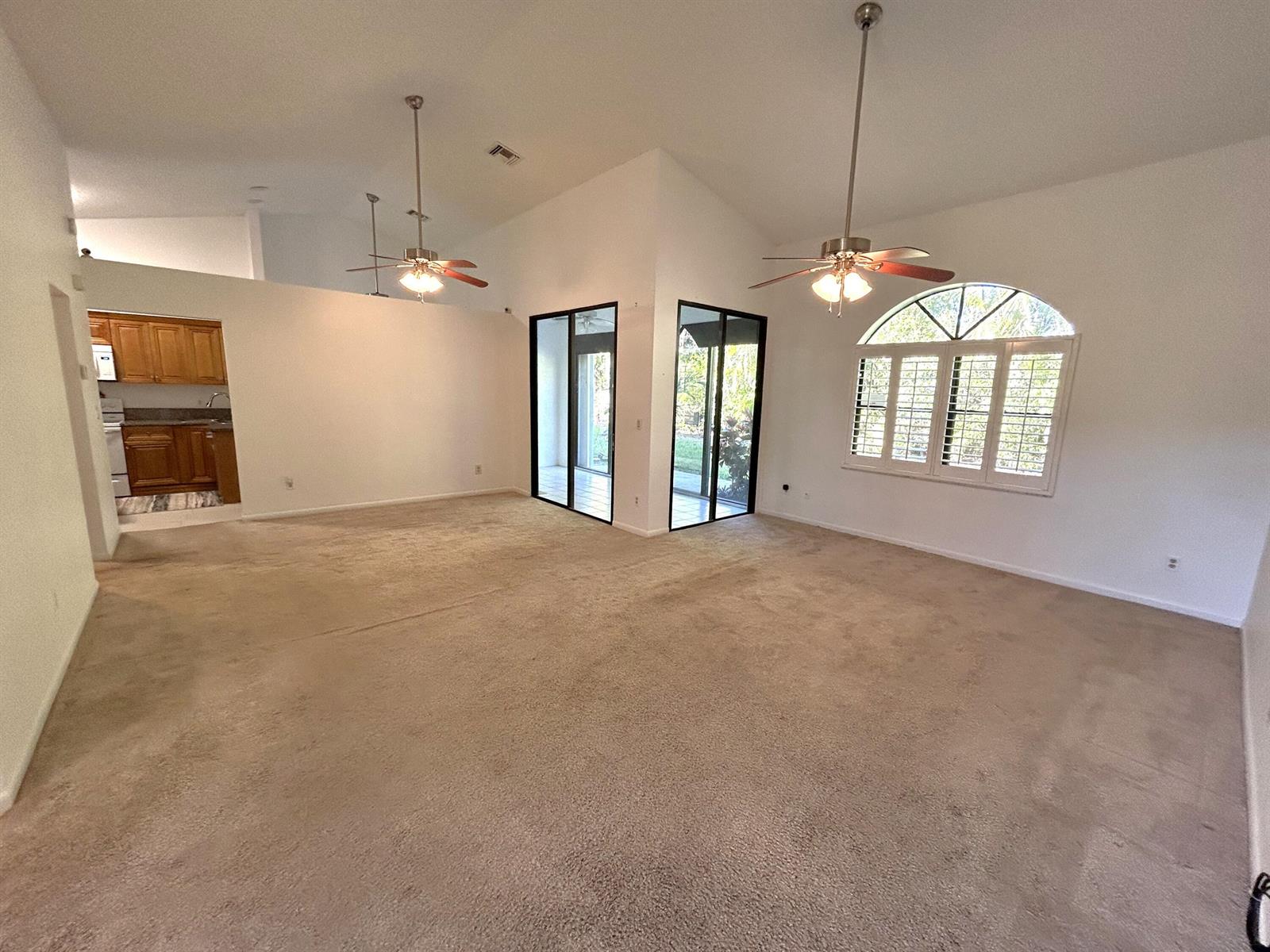 A spacious living room features beige carpeting, vaulted ceilings, two ceiling fans, and sliding doors — 7207 Le Chalet Boulevard, Boynton Beach FL 33472, BOYNTON BEACH, FL