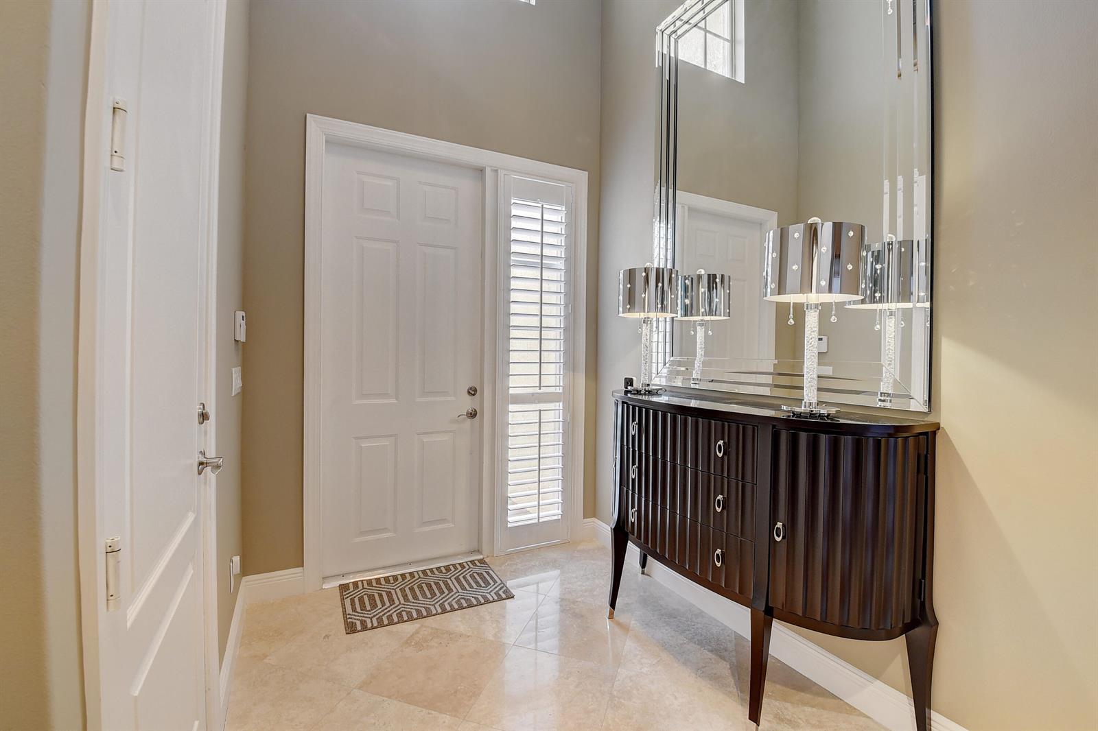 A foyer with a dark wood console table, large mirror, and light-colored tile flooring — 5645 NE Trieste Way, Boca Raton FL 33487, BOCA RATON, FL