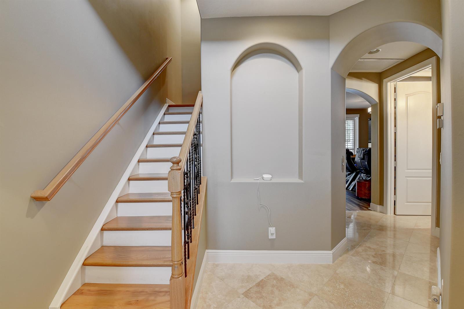 A staircase with wood treads and iron railings sits beside an arched wall niche — 5645 NE Trieste Way, Boca Raton FL 33487, BOCA RATON, FL