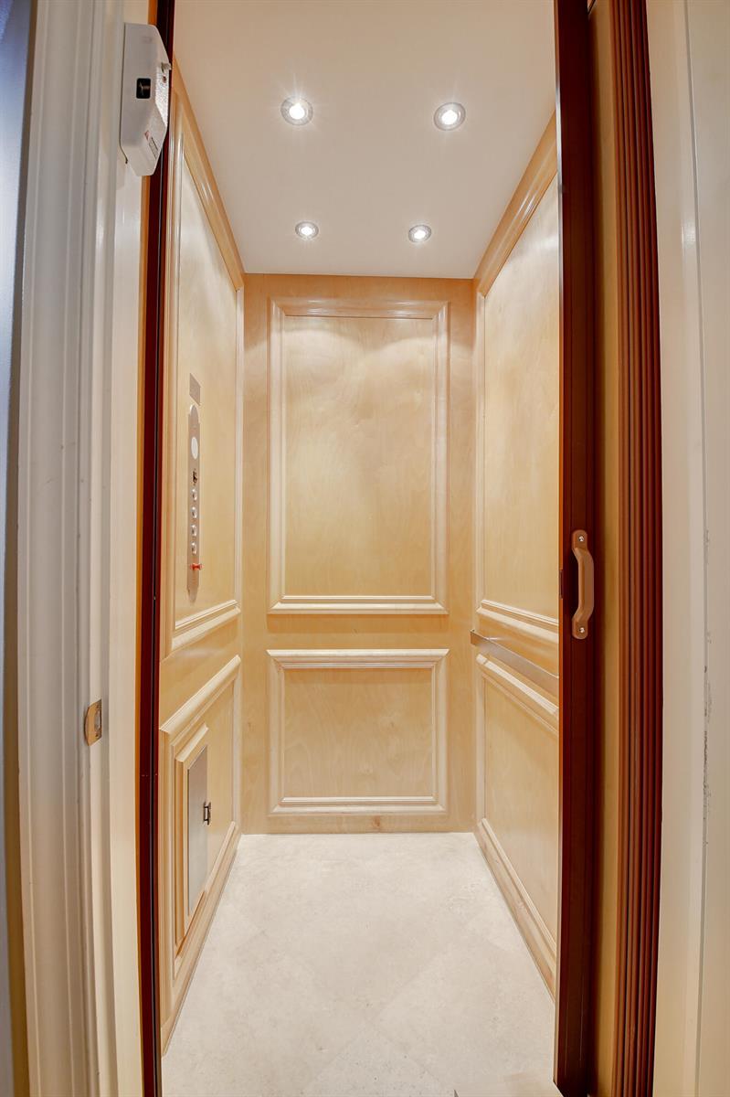 A residential elevator with light wood paneling, recessed ceiling lights, and a stone floor — 5645 NE Trieste Way, Boca Raton FL 33487, BOCA RATON, FL