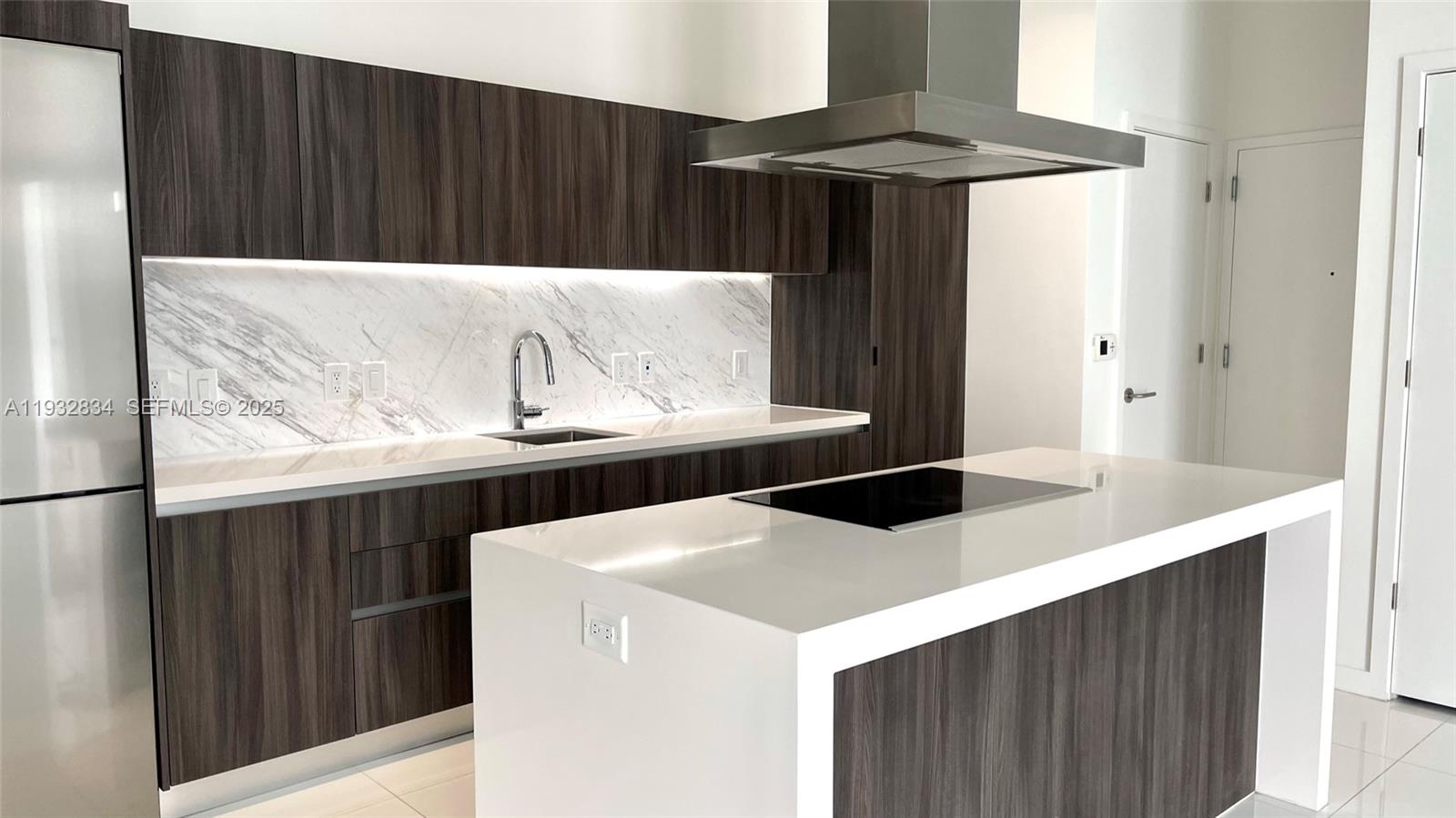 A modern kitchen features dark wood cabinetry, white marble backsplashes, and a white island — 851 NE 1st Ave # 412, Miami FL 33132, MIAMI, FL