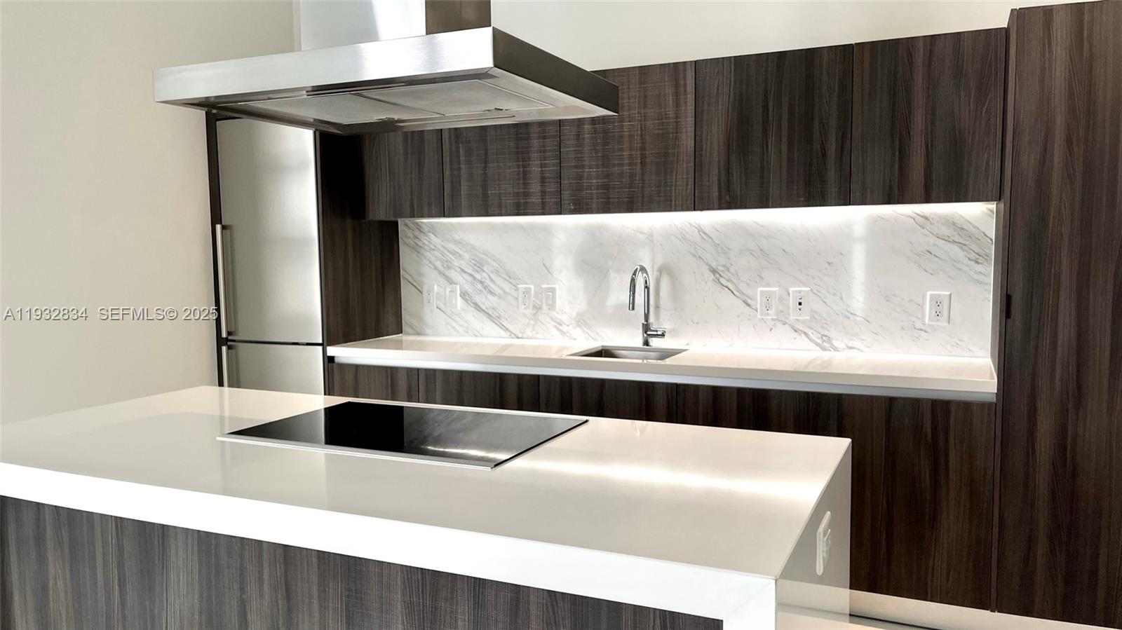 A modern kitchen features dark wood cabinetry, white marble-patterned backsplash, and a white island — 851 NE 1st Ave # 412, Miami FL 33132, MIAMI, FL