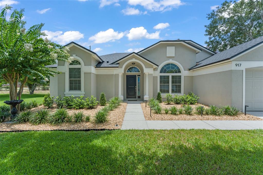 A single-story house with a beige stucco exterior, arched windows, and a gravel front yard — 917 VIA BIANCA DRIVE, DAVENPORT, FL