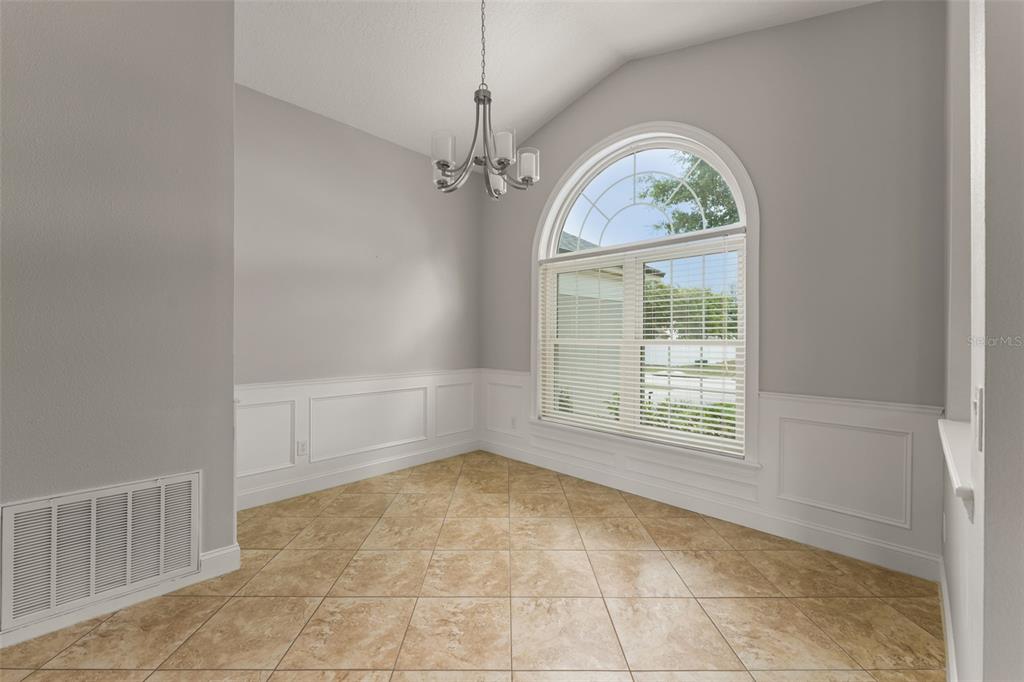 A dining room features tile flooring, white wainscoting, a chandelier, and an arched window — 917 VIA BIANCA DRIVE, DAVENPORT, FL