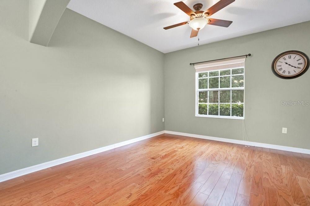 An empty room with light green walls, hardwood floors, a ceiling fan, and a wall clock — 4847 HAVILLAND DRIVE, MOUNT DORA, FL