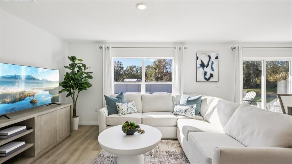 A bright living room features a white sectional sofa, a round coffee table, and television — 1210 ALPINE ASH PLACE, RUSKIN, FL