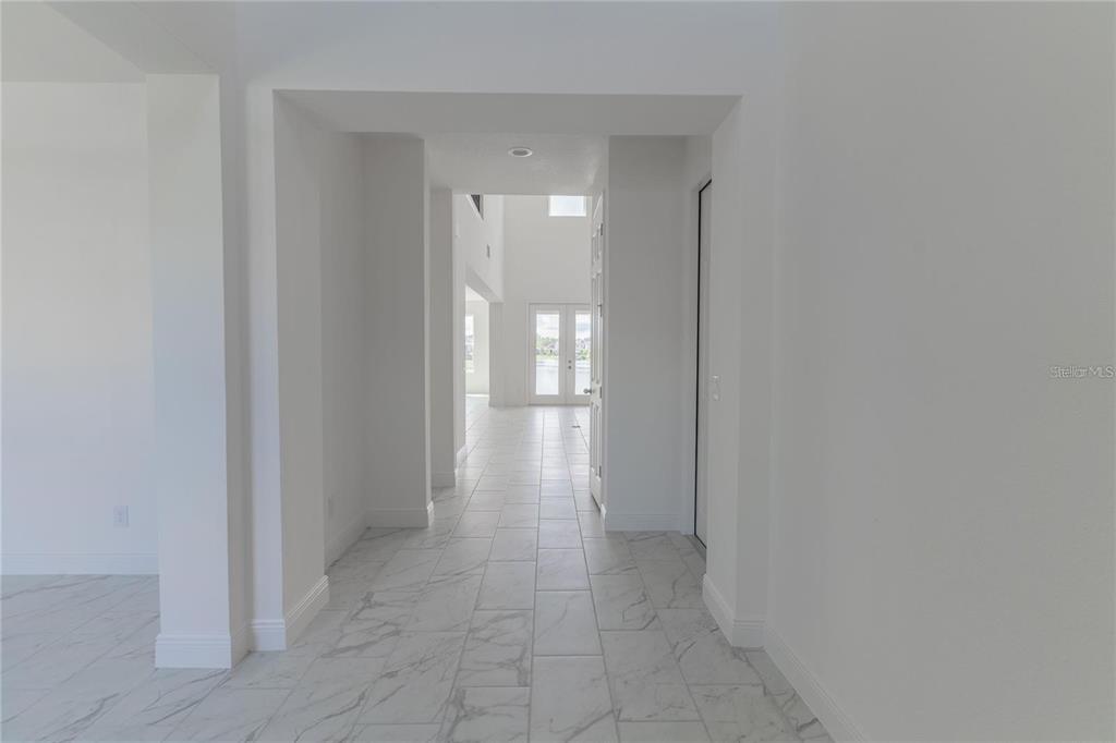 A white-walled hallway with marble-look tile flooring leads toward a bright, open living area — 5018 DOWN COURT, ST CLOUD, FL