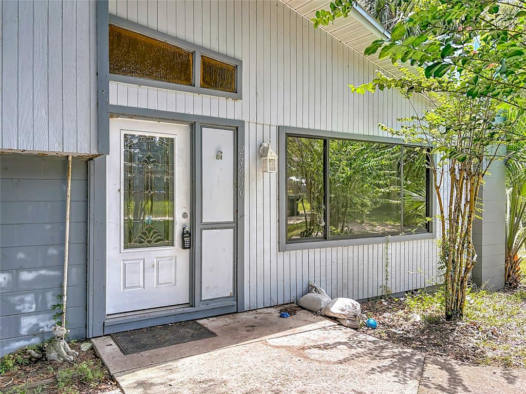 The exterior of a house features a white front door, vertical siding, and a large window — 24930 AVENUE C, PAISLEY, FL