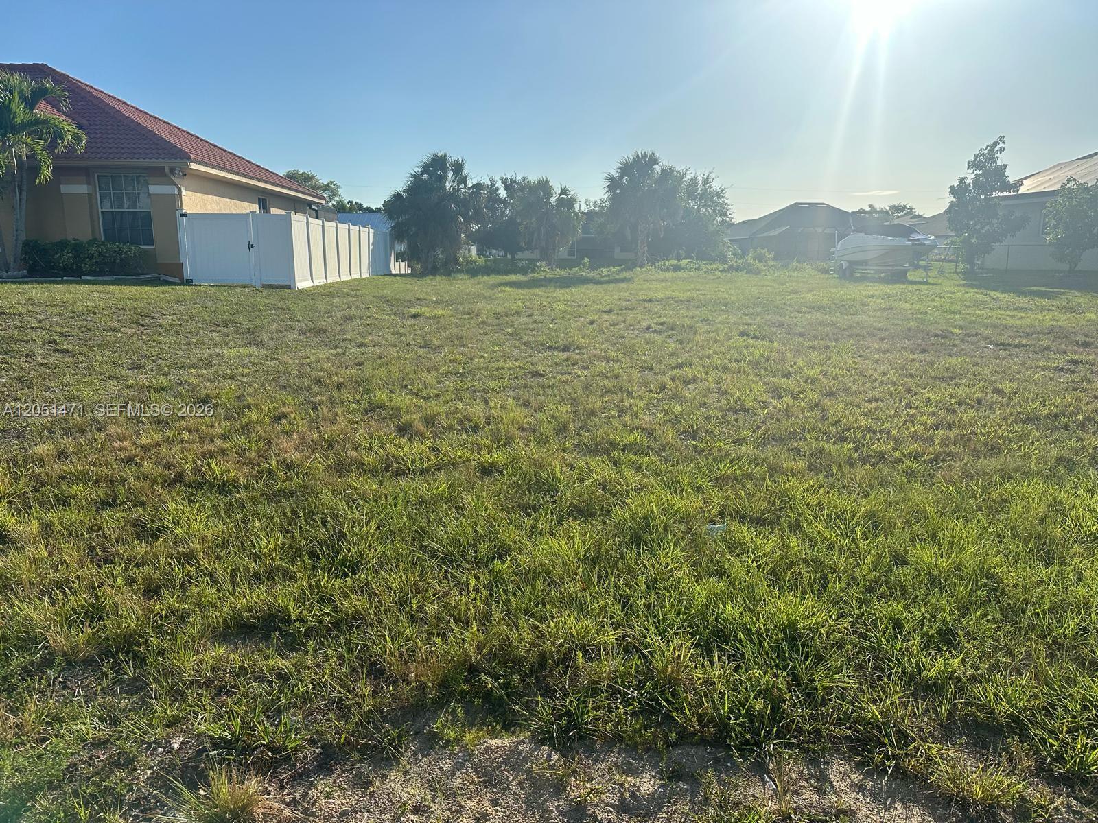 A grassy, vacant residential lot sits next to a house with a white fence — 930 SW 8th PL, Cape Coral FL 33991, CAPE CORAL, FL