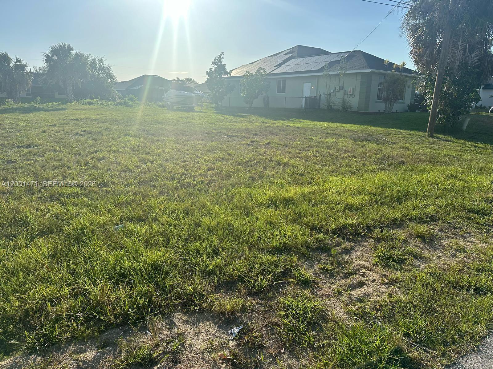 A grassy vacant lot sits in front of a house with solar panels on the roof — 930 SW 8th PL, Cape Coral FL 33991, CAPE CORAL, FL