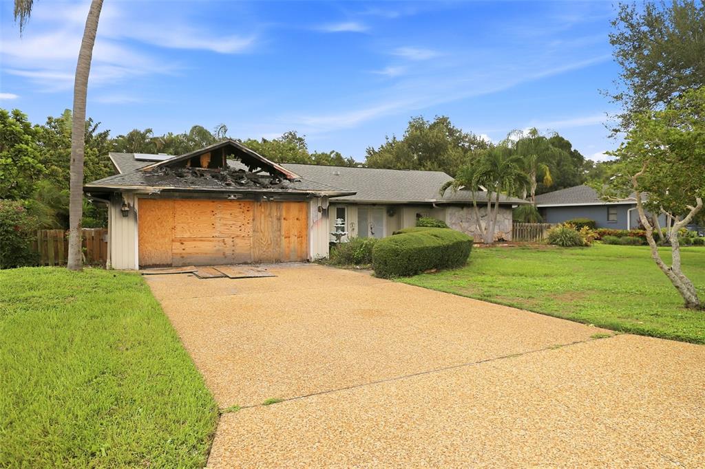 A single-story house with a fire-damaged garage and boarded-up doors sits on a grassy lot — 3745 COUNTRYSIDE ROAD, SARASOTA, FL