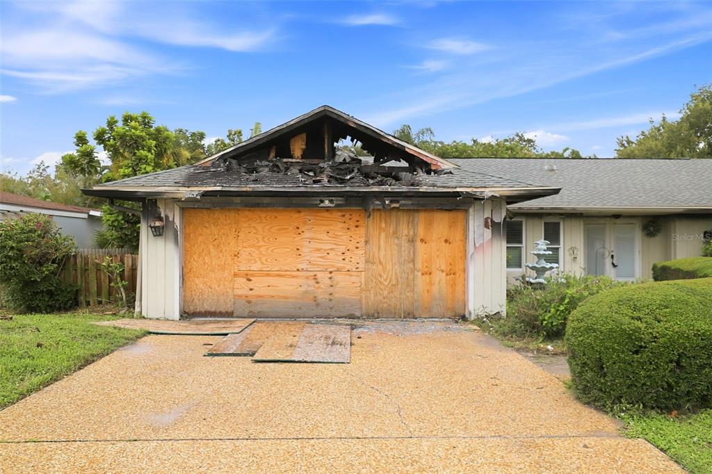 A single-story house with a fire-damaged roof and plywood covering the garage door — 3745 COUNTRYSIDE ROAD, SARASOTA, FL