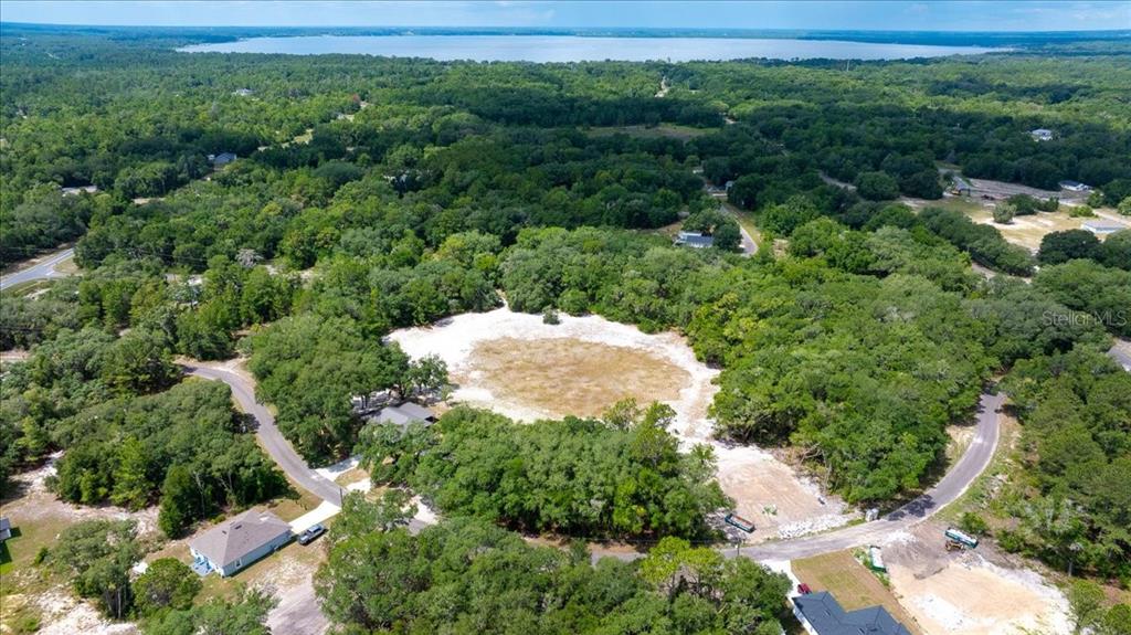 An aerial view shows a cleared, sandy lot surrounded by dense trees near a lake — FISHER LANE COURT, OCKLAWAHA, FL