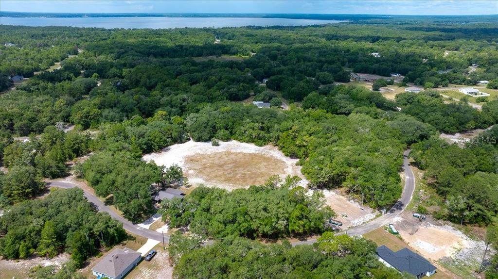 An aerial view shows a cleared, sandy lot surrounded by dense trees near a lake — FISHER LANE COURT, OCKLAWAHA, FL