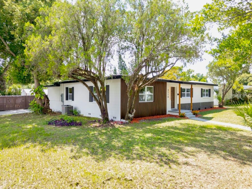 A single-story house with white and wood-paneled siding sits behind a large tree — 3118 PICKFAIR STREET, ORLANDO, FL