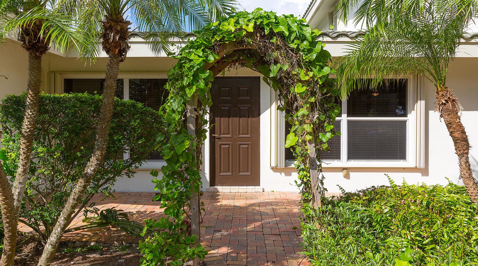 A brown front door is framed by a vine-covered wooden arch on a brick patio — 2003 Bay Drive, Pompano Beach FL 33062, POMPANO BEACH, FL