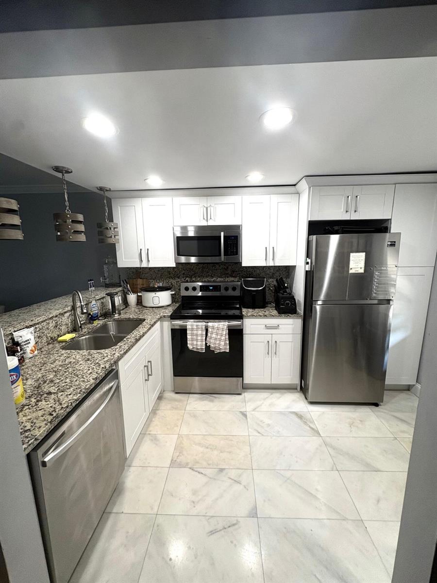 A kitchen features white cabinets, granite countertops, stainless steel appliances, and light-colored tile flooring — 605 Oaks Drive # 304, Pompano Beach FL 33069, POMPANO BEACH, FL