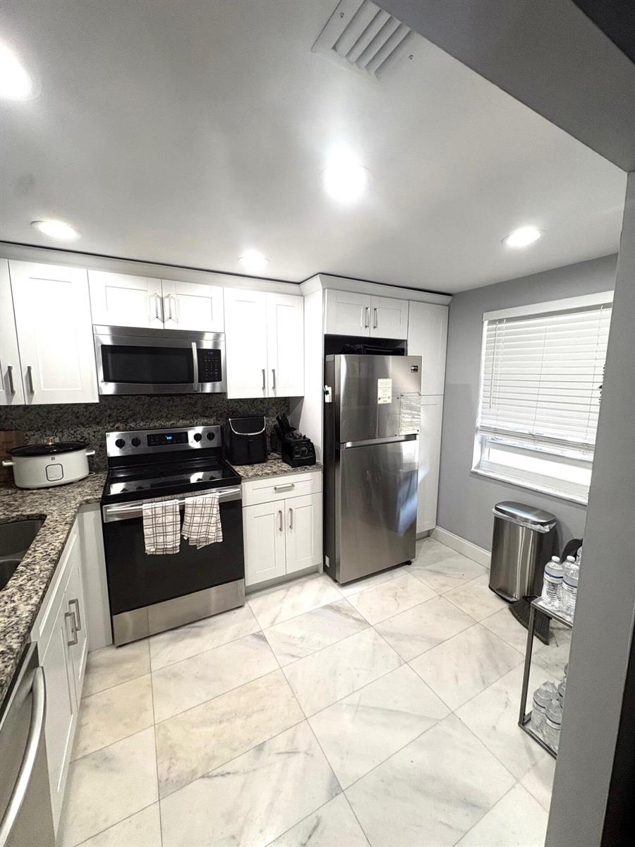 A kitchen with white cabinets, stainless steel appliances, granite countertops, and light-colored tile flooring — 605 Oaks Drive # 304, Pompano Beach FL 33069, POMPANO BEACH, FL