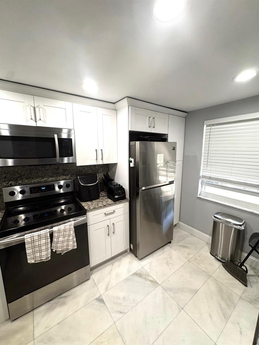 A kitchen features white cabinets, stainless steel appliances, granite countertops, and light-colored tile flooring — 605 Oaks Drive # 304, Pompano Beach FL 33069, POMPANO BEACH, FL