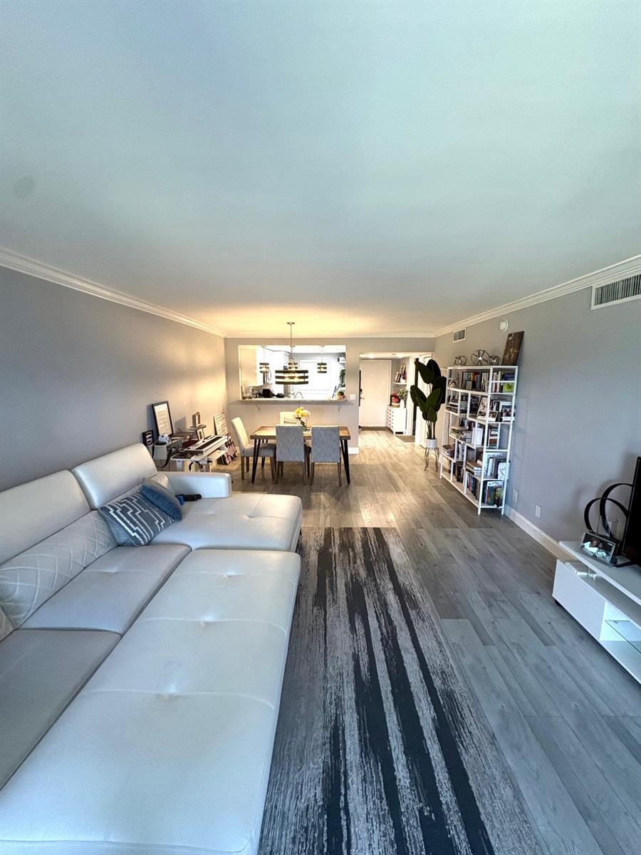 A living room with a white sectional sofa, grey wood floors, and an adjacent dining area — 605 Oaks Drive # 304, Pompano Beach FL 33069, POMPANO BEACH, FL