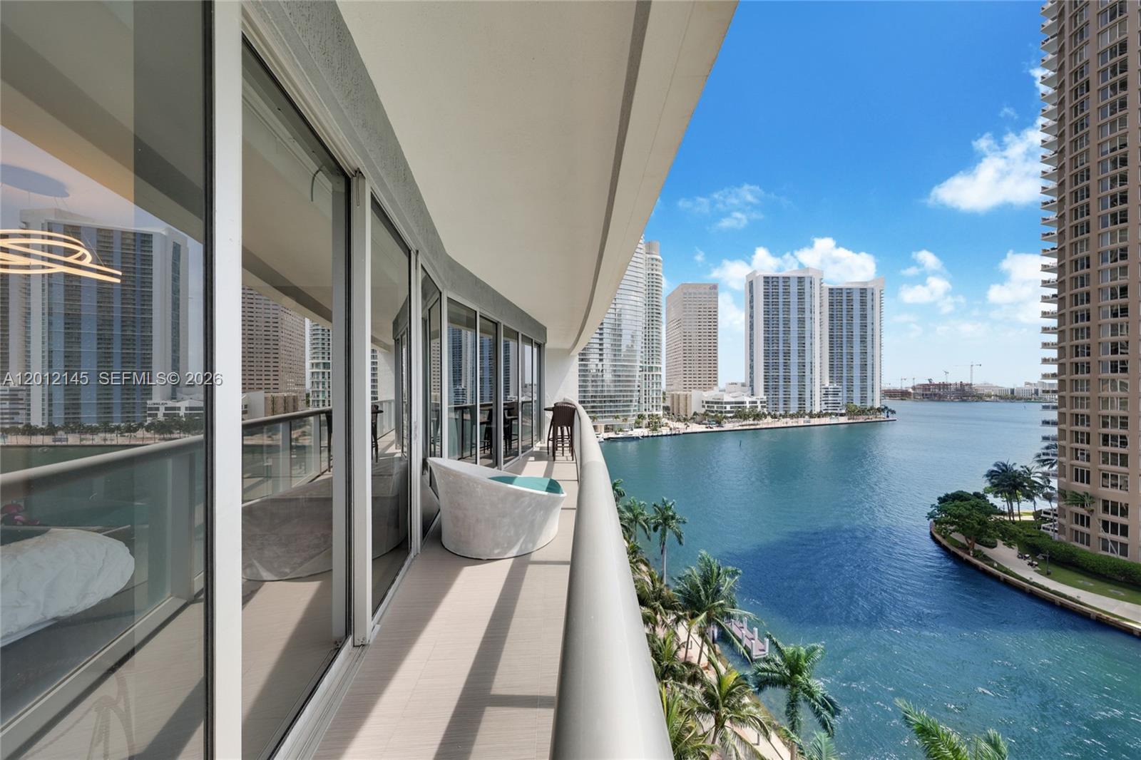 A high-rise balcony overlooks a bay with city skyline views and features a white chair — 465 Brickell Ave # 1019, Miami FL 33131, MIAMI, FL