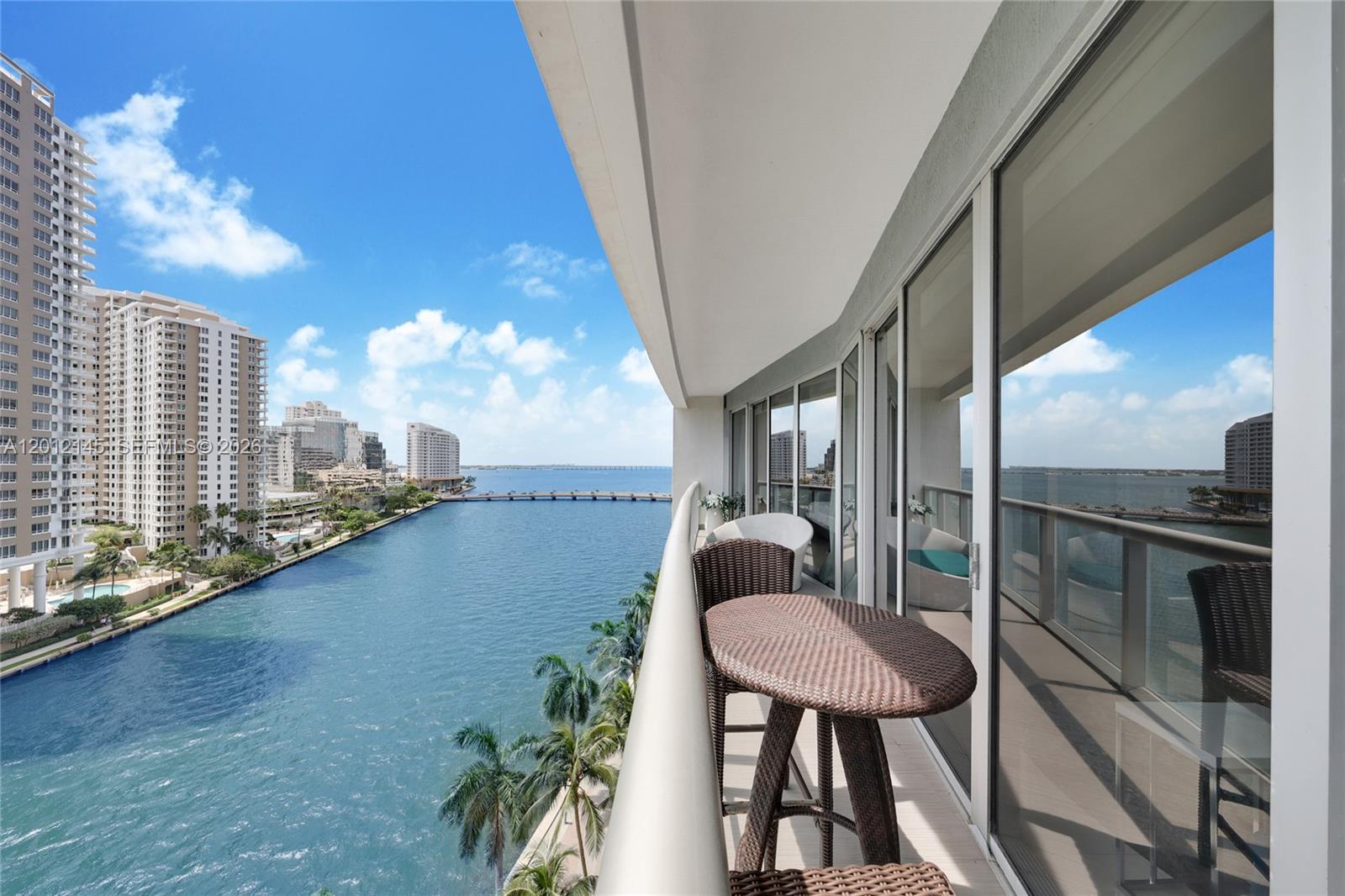 A balcony with wicker furniture overlooks a waterway, a bridge, and high-rise buildings — 465 Brickell Ave # 1019, Miami FL 33131, MIAMI, FL